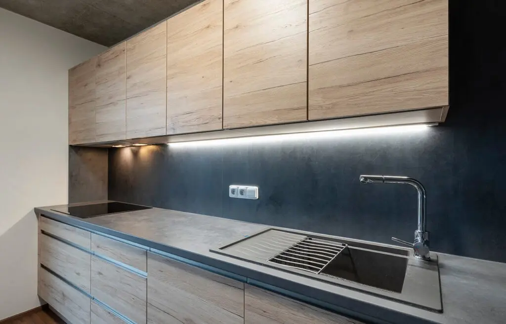 Moderní kuchyňská deska z betonu s dřevěnými skříněmi a umyvadlem.