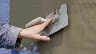 Ruka nanáší lepidlo na fasádu pomocí stěrky.