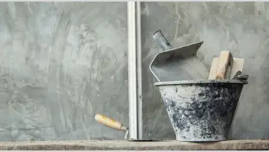 Nástroje pro omítání v kbelíku na pozadí betonové stěny.