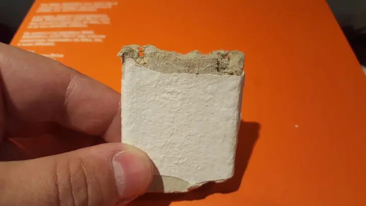 Rozbitý vzorek bílého stavebního materiálu s viditelnými vlákny.