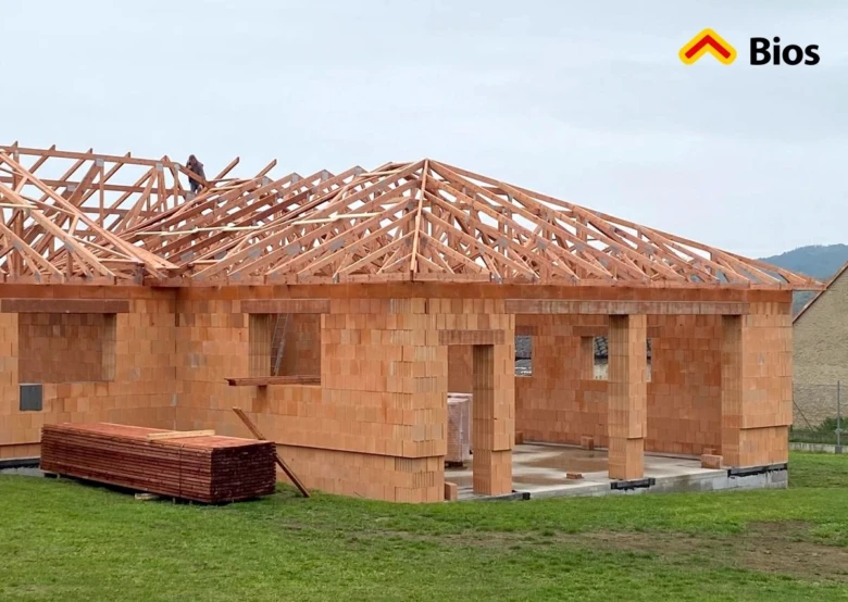 Montáž vazníků valbové střechy na stavbě domu s cihlovými zdmi.