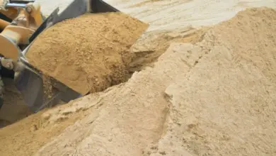 Žlutý nakladač s košem plným suchého písku na stavbě.