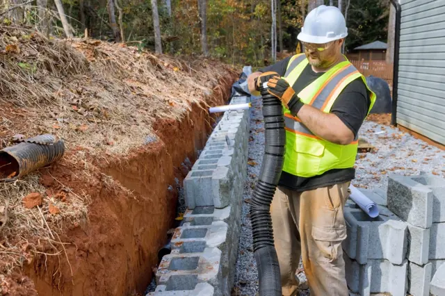 Stavebník připravuje základ pro betonovou opěrnou zeď.