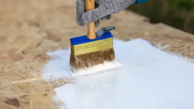 Ruční natírání OSB desky bílou barvou štětcem.