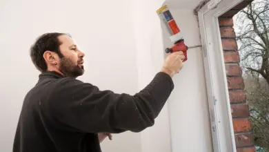 Muž nanáší montážní pěnu kolem okenního rámu.