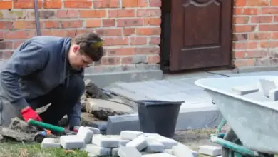 Muž klade dlažební kostky u základů starého domu.