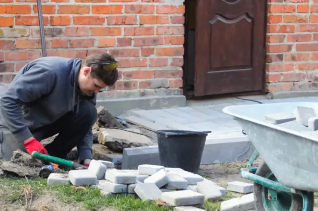 Muž klade dlažební kostky u základů starého domu.