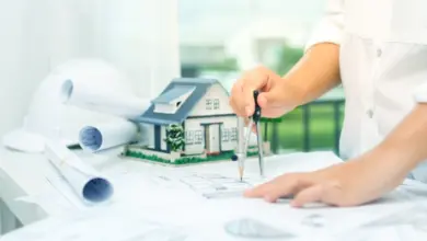 Architekt kreslí plány vedle modelu domu s kompasem.