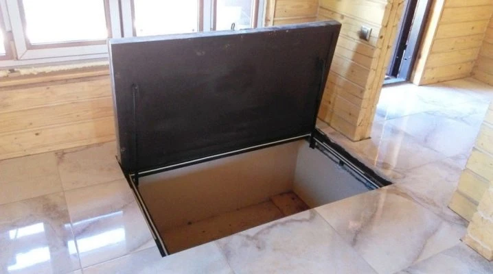Otevřený poklop do suterénu v dlažbě uvnitř dřevěného domu.