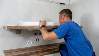 Muž instaluje umyvadlo na dřevěný polic v koupelně.