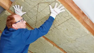 Muž instaluje minerální vlnu mezi trámy ve střeše.