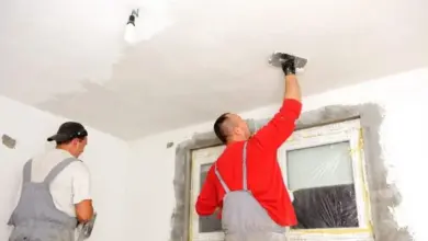 Dva muži opravují strop v interiéru pomocí špachtle.