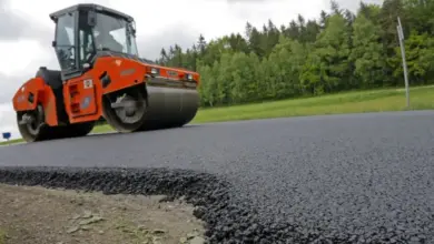 Oranžový válec utěsnuje čerstvý asfalt na nové silnici.