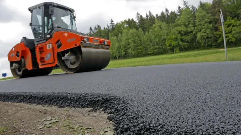 Oranžový válec utěsnuje čerstvý asfalt na nové silnici.