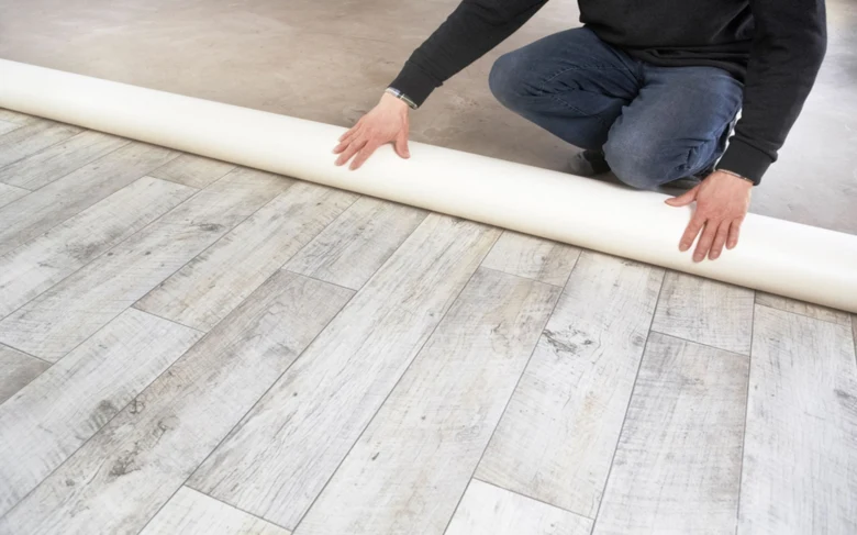 Muž rozkládá podkladovou fólii pro linoleum na dřevěnou podlahu.