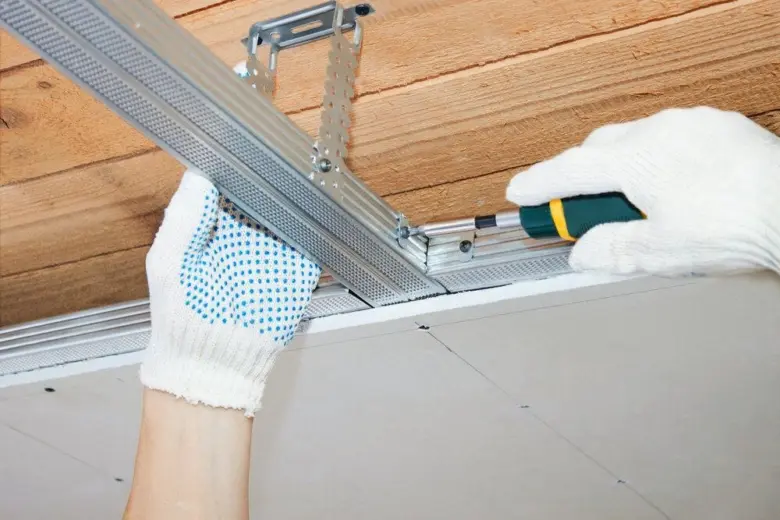 Ruční instalace kovového profilu pro sádrokarton na dřevěné trámy.