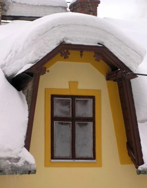 Žlutá střecha domu s oknem pod tlustou vrstvou sněhu.