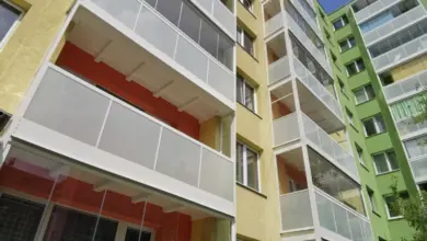Nově instalované skleněné přístavby balkonů na žluté fasádě bytového domu.
