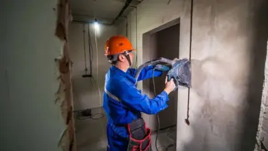 Stavebník v modrém obleku děrá stěnu pro instalaci kabeláže.