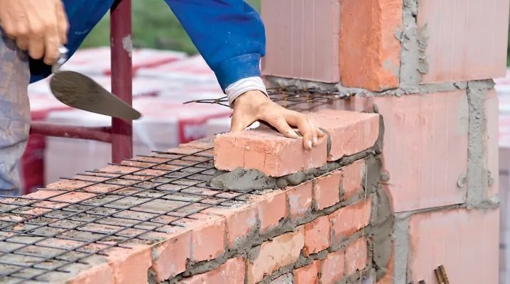 Stavebník kladne cihlu na maltu do zdiva s ocelovou výztuhou.