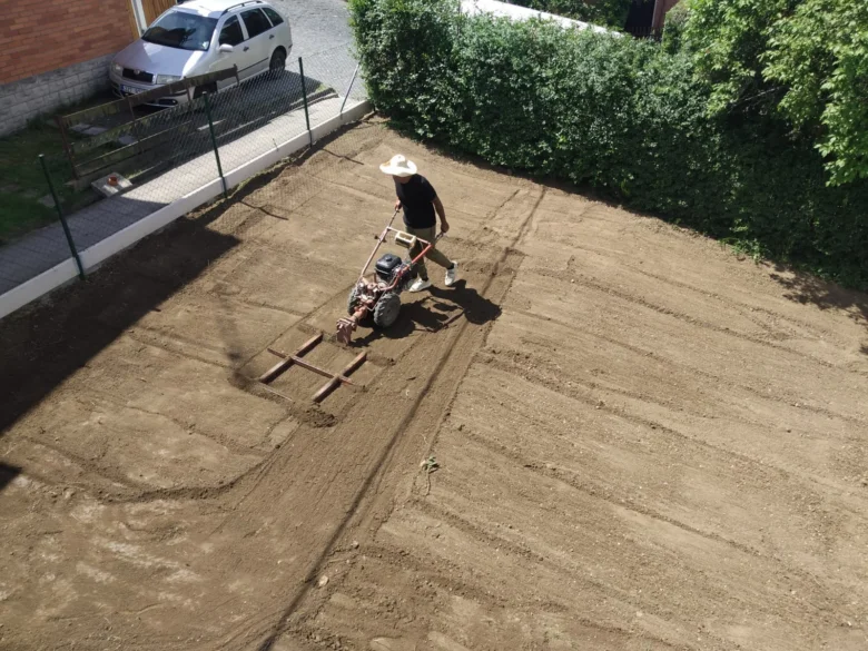 Muž vyrovnává pozemek motokultivátorem na zahradě.