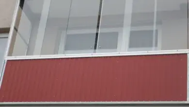 Zasklení balkonu sklem v hliníkovém profilu na červené fasádě.
