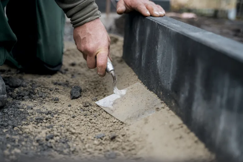Kladení obrubníku s maltou rukama pracovníka