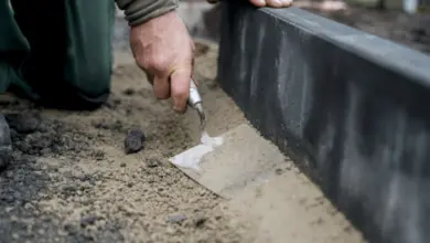 Ruce člověka nanášejí maltu na okraj betonového obrubníku venku.