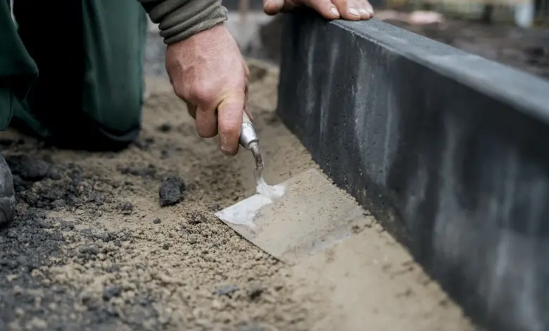 Ruce člověka nanášejí maltu na okraj betonového obrubníku venku.