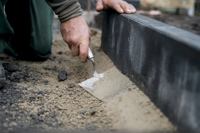 Ruce člověka nanášejí maltu na okraj betonového obrubníku venku.