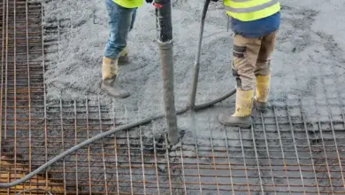 Dva dělníci nalévají beton na ocelovou mřížku.