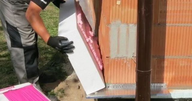 Montážní pracovník připevňuje panel z expandovaného polystyrénu na kovovou stěnu.
