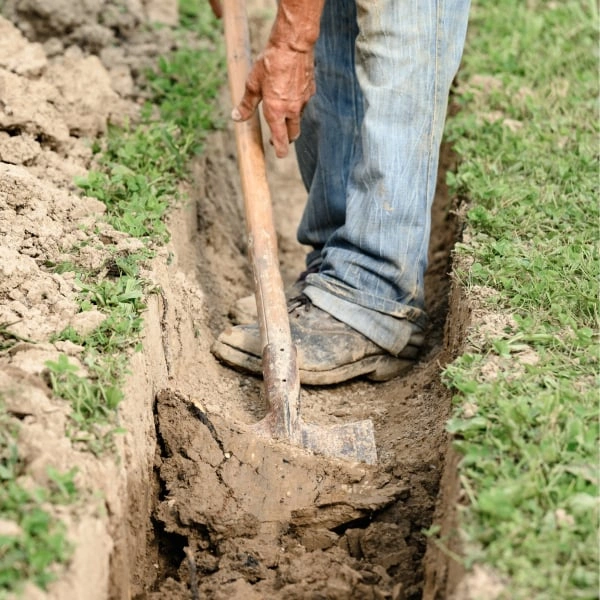 Muž kopá příkop lopatou pro drenáž kolem domu.