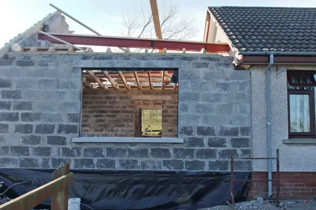 Přístavba domu s kamennou zdí a oknem ve fázi stavby.