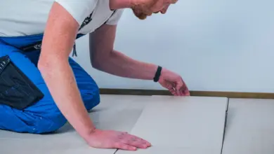 Muž kladou dlaždici na podlahu během instalace obkladů.