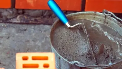 Kbelík s maltou a kladivo vedle cihly pro zdivo.
