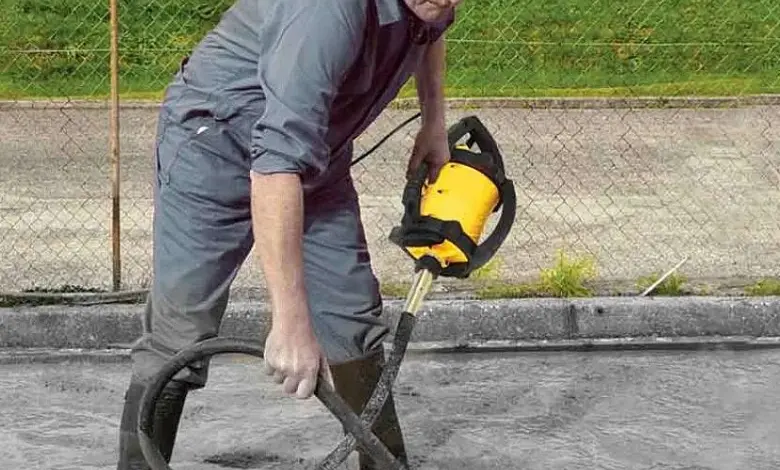 Muž vibruje čerstvý beton žlutým vibračním nástrojem.