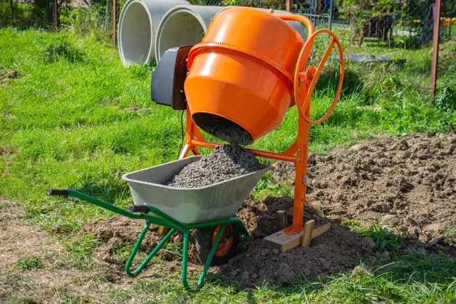 Oranžová betonova míchačka nalévá směs do vozíku na staveništi.