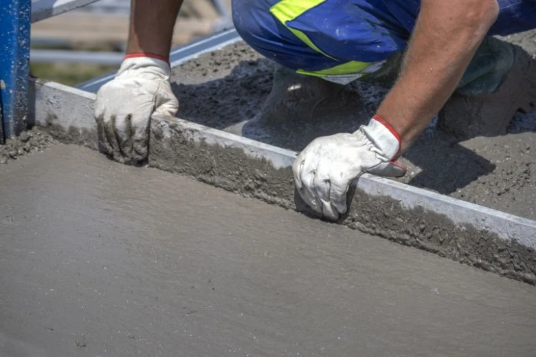 Stavebník vyrovnává čerstvý beton na podlaze pomocí pravítka.