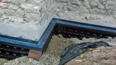 Černá drenážní fólie pod kamennou zdí s štěrkem.