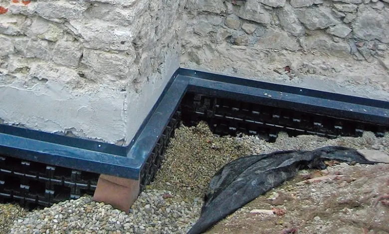 Černá drenážní fólie pod kamennou zdí s štěrkem.