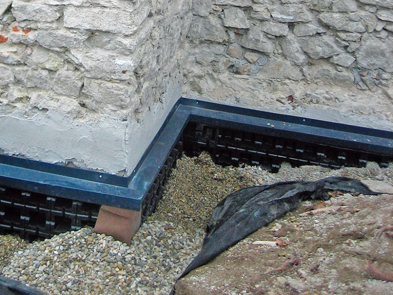 Černá drenážní fólie pod kamennou zdí s štěrkem.