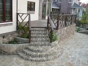 Kamenné schody vedoucí k dřevěné terase u cihlového domu.
