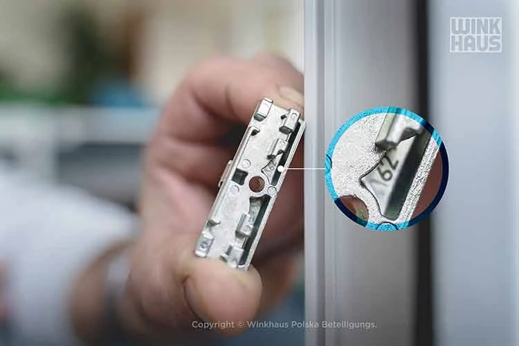 Ruka drží kovový díl plastového okna s detailním záběrem na mechanismus.