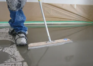 Pracovník rozšiřuje samonivelační podlahu pomocí široké špachtle.