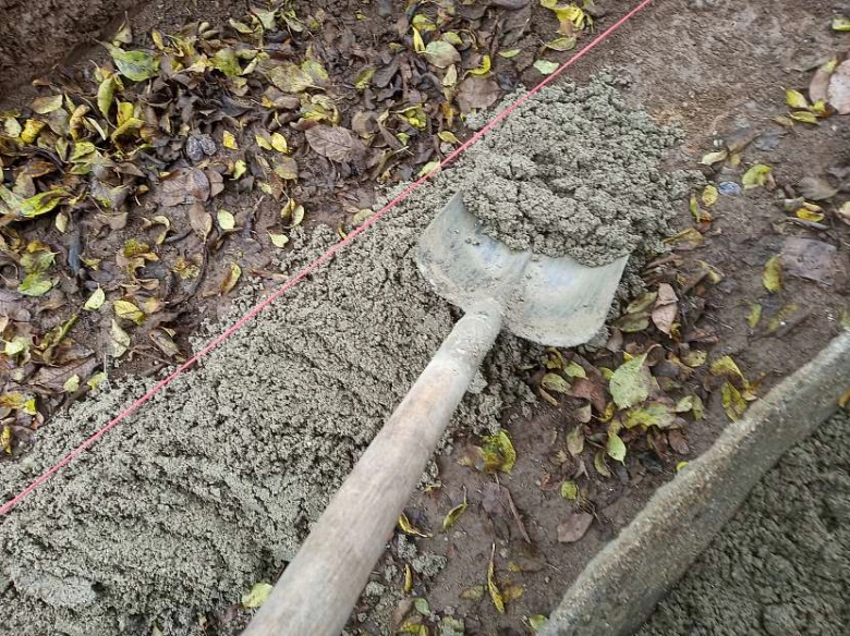 Lopata s čerstvým betonem pro instalaci obrubníku na zemi.