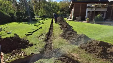 Muž kopá příkop pro odvodnění trávníku vedle domu.