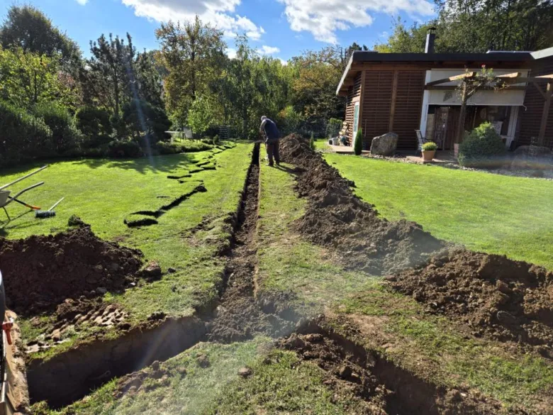 Muž kopá příkop pro odvodnění trávníku vedle domu.