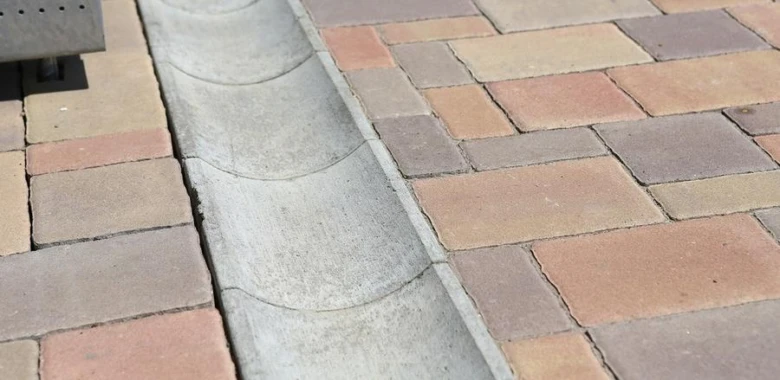 Konkrétní drenážní žlóbek mezi dlaždicemi na zahradě.