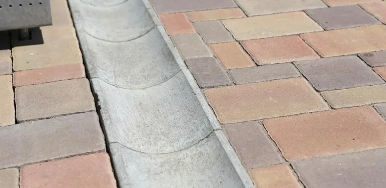Konkrétní betonový odvodňovací žlóbek vedle dlažby.